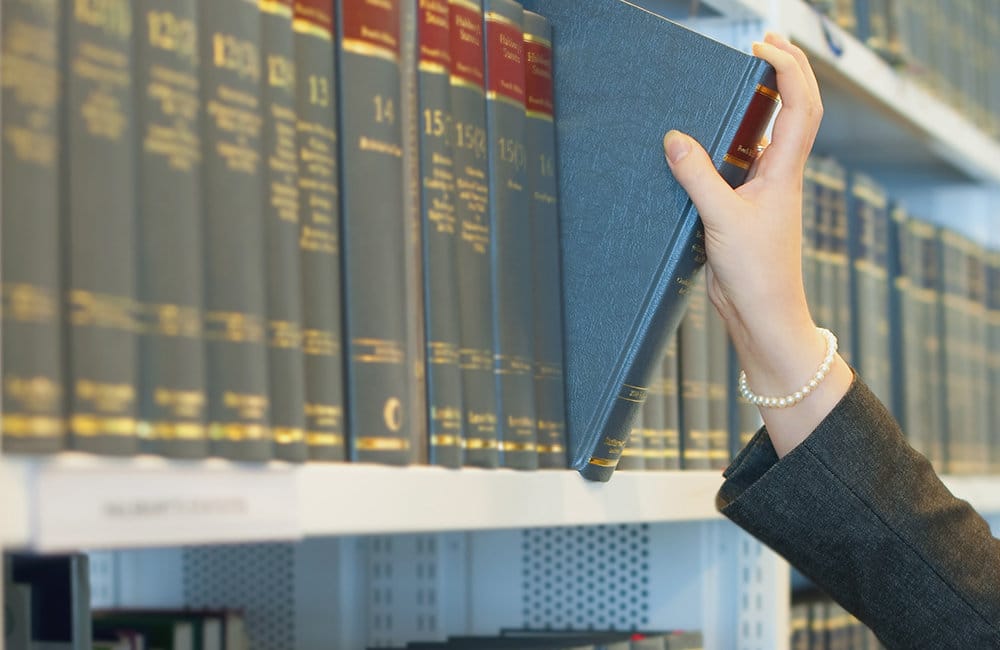 Caucasian businesswoman pulling book from law library shelf