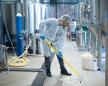 Fabrikada büyük bir makine ve onu temizleyen beyaz tulum giymiş bir adam Fabrikada büyük bir makine ve onu temizleyen beyaz tulum giymiş bir adam